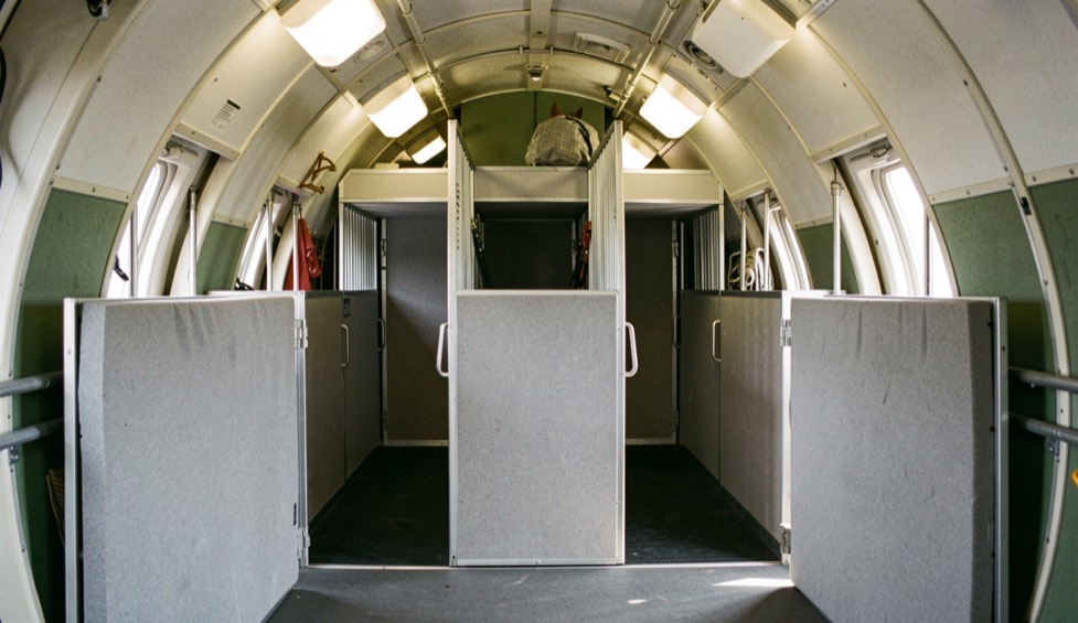 Empty three horse jet stall inside an aircraft hold with partition walls folded back and foam padding on the front gates under strip lighting